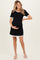 woman wearing a black maternity dress with white ruffle details and holding her baby bump