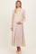 woman wearing a cream ribbed maternity sweater and a pale pink maxi skirt, gently holding her baby bump