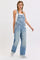 woman wearing light blue oversized denim overalls with a white tank top underneath and braids in her hair
