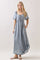 woman wearing a light blue denim maxi dress with puff sleeves and a square neckline, featuring a tie detail and pockets