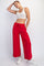 woman wearing a white crop top and red wide-leg sweatpants, posing with one hand on her hip and wearing white sneakers
