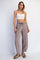 woman wearing a white crop top and taupe loose-fitting pants, standing with hands on her sides
