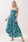 woman wearing a teal strapless maxi dress with floral patterns and a fitted bodice, standing on a neutral background