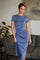 woman wearing a blue short sleeve midi dress with a side slit, standing in a modern living space