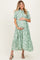 woman wearing a green floral print maternity dress and cradling her baby bump