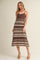 woman wearing a brown and cream striped midi dress with spaghetti straps and a tiered hem, standing in a neutral background