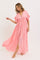 woman wearing a pink maxi dress with ruffled sleeves and a tie front detail, standing in a flowing pose