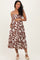 woman wearing a brown and white patterned maternity dress, holding her baby bump with a smile