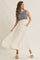woman wearing a sleeveless blue knit and white maxi dress with a flowy skirt and pockets, standing against a neutral background