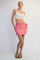 woman wearing a white crop top and a pink athletic skirt with pockets, standing against a light background