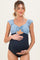 woman wearing a blue and navy maternity swimsuit with ruffle sleeves and a knot detail, holding her baby bump
