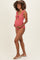 woman wearing a pink maternity swimsuit with ruffle straps and a tie front, holding her baby bump