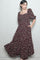 woman wearing a burgundy floral maxi dress with puff sleeves and a ruffled hem, posing with one hand in pocket