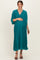 woman wearing a teal pleated maternity dress, gently cradling her baby bump