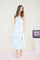 woman wearing a light blue floral midi dress with pockets, standing against a soft backdrop