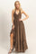 woman wearing a brown halter neck maxi dress with a tie front and ruffled hem, posing with one leg slightly exposed