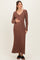 woman wearing a long brown ribbed maternity dress with a v-neck and tie waist, gently cradling her baby bump