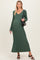 woman wearing a dark green maternity maxi dress with ribbed detailing and a tie waist, carrying a black handbag