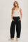 woman wearing a cream ribbed tank top and black wide-leg trousers, standing with hands in pockets