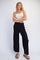 woman wearing a white tank top and black wide-leg pants, standing with arms crossed and wearing sandals