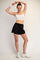 woman wearing a white sports bra and black athletic shorts, posing with one arm raised and smiling