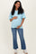woman wearing a light blue short sleeve maternity top and distressed jeans, showing her baby bump with a smile