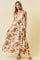 woman wearing a white maxi dress with brown floral prints and spaghetti straps, standing against a light beige background