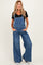 woman wearing a dark blue denim maternity overall jumpsuit with wide legs and a black short sleeve top, no baby bump visible