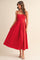 woman wearing a red sleeveless midi dress with a square neckline and pleated skirt, standing against a neutral background