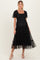 woman wearing a black maternity dress with puff sleeves and tiered skirt, showcasing her baby bump