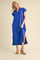 woman wearing a bright blue short sleeve maxi dress with a polo-style collar and side slits, standing in wedge sandals