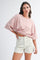 woman wearing a pink striped oversized t-shirt with knotted detail and cream-colored denim shorts
