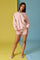 woman wearing a light pink oversized sweatshirt and floral print shorts, standing against a colorful backdrop