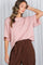 woman wearing a blush oversized short sleeve top with relaxed fit and brown high-waisted wide-leg pants