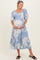 woman wearing a light blue floral maternity dress with puff sleeves, holding her baby bump