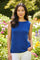 woman wearing a bright blue sleeveless top and white pants standing in a flower garden