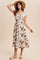 woman wearing a cream floral midi dress with ruffled sleeves and a smocked waist, accessorized with a straw hat