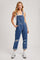 woman wearing a light blue distressed denim overalls with rolled cuffs and a white tank top underneath