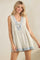 woman wearing a floral print sleeveless romper with a v-neck and tie detail, in soft beige and blue colors
