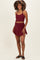 woman wearing a burgundy maternity crop top and matching skirt with a sporty style, no visible baby bump