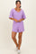 woman wearing a lavender short sleeve romper with a v-neckline and pockets, standing against a neutral background