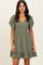 woman wearing an olive green short puff sleeve dress with a smocked bodice and ruffle hem