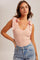 woman wearing a light pink sleeveless top with tie details on the shoulders and high-waisted denim shorts