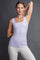 woman wearing a light purple square neck tank top paired with white pants, posing with one arm raised