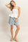 woman wearing a white strapless peplum top and light blue shorts, standing with one hand on her hip