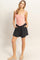 woman wearing a pink ruffled tank top and black shorts, posing with hands in pockets