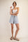 woman wearing a white crop top and light blue drawstring shorts, posing with one hand on her hip