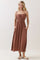 woman wearing a rust-colored maxi dress with spaghetti straps and pockets, smiling at the camera