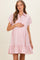 woman wearing a light pink maternity shirt dress with short sleeves and ruffle hem, holding her baby bump