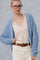 woman wearing a light blue cable knit cardigan over a beige lace cami top and white high-waisted pants with a leopard print belt
